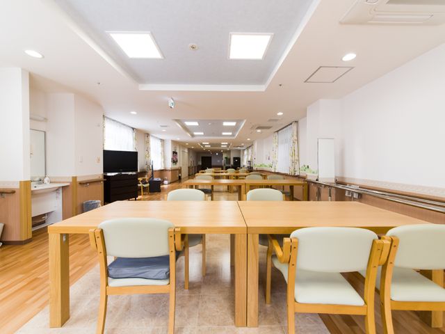 広々とした明るい食堂 ホール 暖かみのある照明と木製のテーブルが並ぶ共有スペースです。ゆったりと食事や交流が楽しめる環境が整っています。