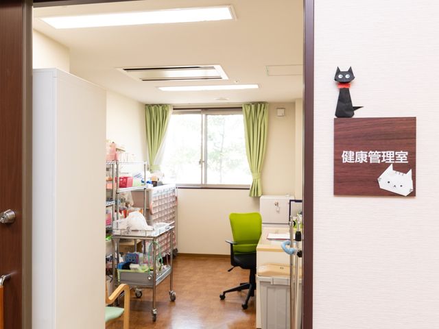 看板付き明るい廊下 健康管理室 機能訓練室への入り口が装飾された廊下です。心地よい自然光が差し込み、温かな雰囲気を醸し出しています。