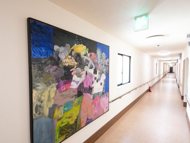 長い廊下と壁の絵画 通路 広々とした廊下は明るく、壁に飾られた絵画が温かみのある雰囲気を醸し出しています。足元には滑りにくい素材を使用しており、安心して歩行できる環境が整っています。