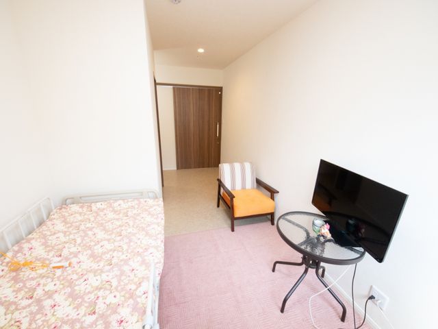 明るい個室の居室 居室 広々とした個室で、ベッドとテレビが備わり、ゆったりとお過ごしいただけます。ソファがあり、訪問者を快適にお迎えできる空間です。
