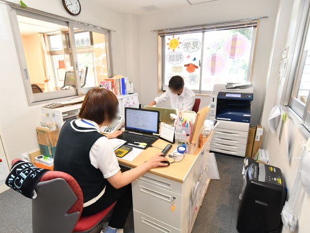 スタッフ業務中のオフィス 事務室 明るく落ち着いたオフィスで、スタッフが日々の業務に取り組んでいます。周囲には必要な備品も整い、効率的なワークスペースが確保されています。