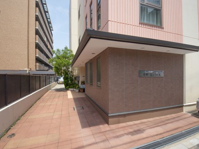 エントランスの壁面と看板 外観 心地よい陽光が差し込む清潔感のあるエントランスです。訪れる方を優しく迎える植栽も配されており、温かな雰囲気が感じられます。