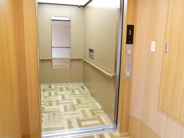 木目調エレベーターの内観 エレベーター 清潔感のあるエレベーター内は、足元に配慮した床材を使用しており、移動のたびに安全と快適さが支えられています。