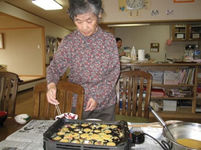 料理をする高齢の女性 レクリエーション風景 心温まる手作りのおやつを提供する広々とした食堂で、笑顔で料理を楽しむ居住者の様子が伺えます。