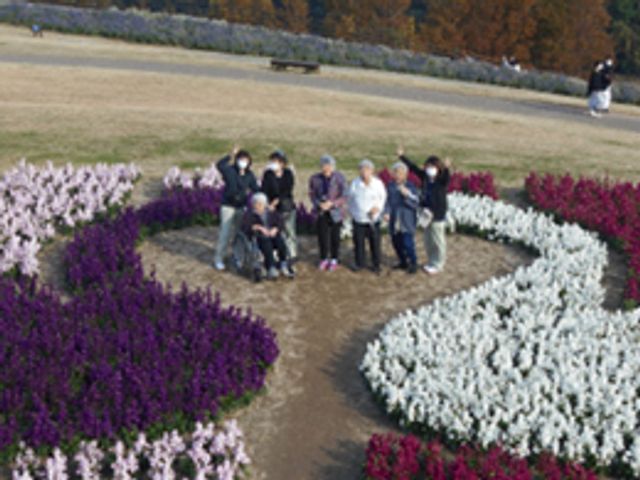 中庭での憩いの時間 中庭 花と緑に囲まれた中庭で、ゆったりとした時を過ごしている様子が伝わります。利用者の皆様が笑顔で寄り添いながら、自然を感じておられます。