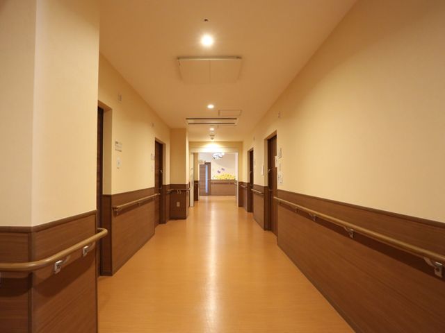 廊下の明るい通路 廊下 手すり付きの広々とした廊下です。落ち着いた色合いで、安全かつ穏やかな雰囲気が保たれています。