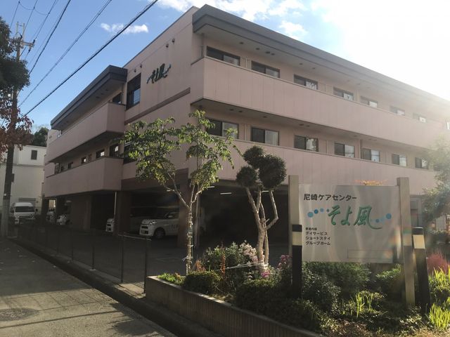 ケアセンター外観 エントランス 温かみのあるピンク色の建物です。入口近くの緑が気持ちを和ませてくれ、働きやすい環境が感じられます。