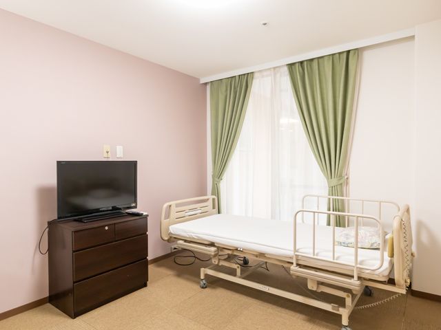 明るい居室 居室 自然光がたっぷり入る明るい空間で、快適な居住環境を提供しています。ベッド横にはテレビもあり、リラックスできる環境です。
