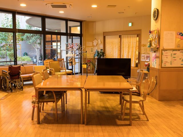 暖かみのあるラウンジ風景 食堂 広々としたラウンジは、木の温もりが感じられ落ち着いた雰囲気です。車椅子も置かれており、ゆったりと時間を過ごせる場所となっています。