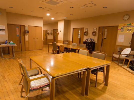 木目調の床の広い食堂がある。居室の並んでいる廊下に通じている。テーブルと椅子がたくさん置かれている。
