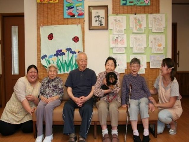 明るい和室での憩いの時 犬 笑顔あふれる居心地の良い和室で、利用者とスタッフが楽しいひとときを共有しています。壁に飾られた手作りの作品が空間に暖かみを加えています。