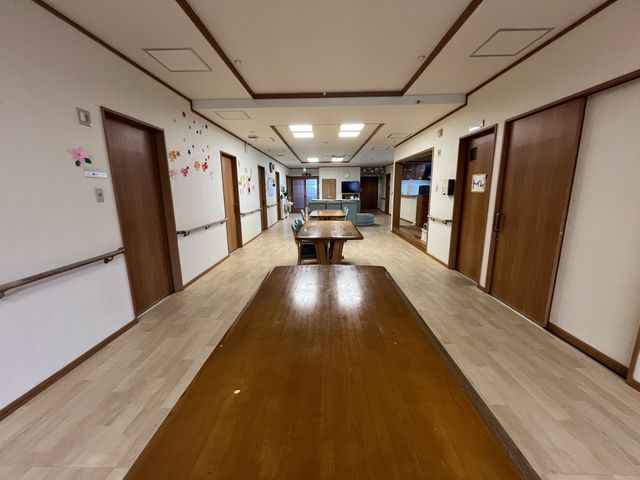 広々とした廊下 廊下 手すり付きの広い廊下が確保されており、安心して歩行できる環境です。壁には飾り絵もあり、温かみのある雰囲気を演出しています。