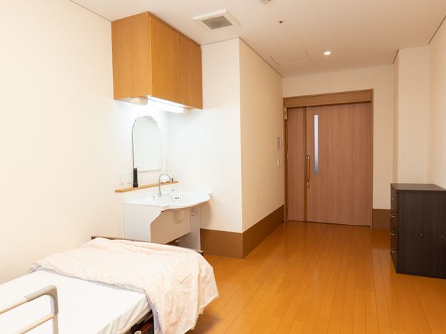 居室のベッドと洗面台 居室 ゆったりとしたスペースの個室で、日々の生活に必要な家具が配備され、落ち着いた雰囲気です。