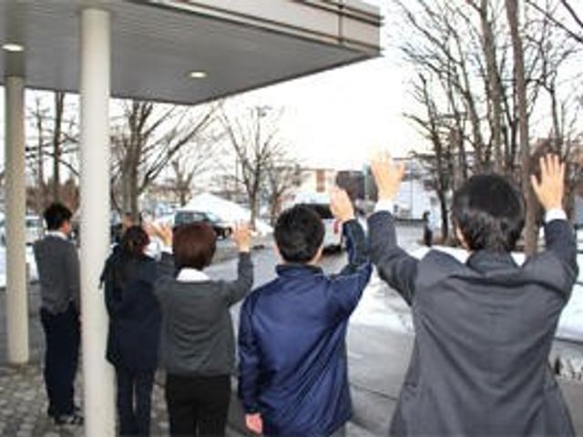 外で手を振る職員たちの外観 外観   建物の前で職員の方々が手を振っており、明るいあいさつが伝わります。出迎えや見送りの雰囲気を感じやすい場面です。