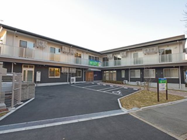 建物前の駐車場外観 外観   2階建ての建物がコの字に配置され、中央に駐車スペースがあります。出入りしやすい動線が見え、働く場の様子をイメージしやすいです。