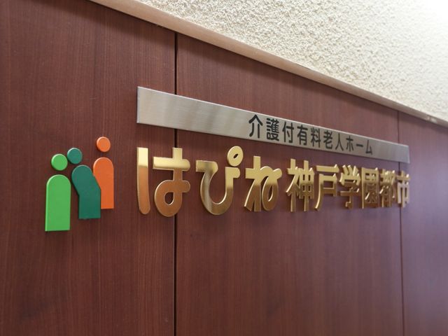 看板のクローズアップ 施設名称プレート 温かみのある色使いの看板が、訪れる人々を優しく迎えてくれます。日々の業務に携わることで、多くの方々の安らぎを支えるやりがいを感じられるでしょう。
