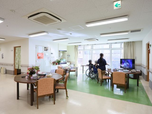 共有スペースの日常風景 共有スペース 明るく広々としたラウンジで、利用者がスタッフと一緒にテレビを観ている様子が見受けられます。日々のリラックスタイムも充実しています。