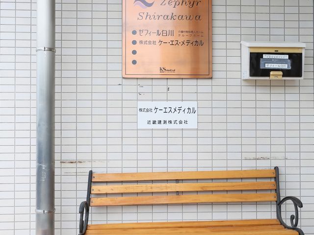 看板とベンチのエントランス 玄関 エレガントな看板が迎える入口には、休憩可能なベンチも完備され、訪れる方々にとって心地よい初めの一歩を提供します。