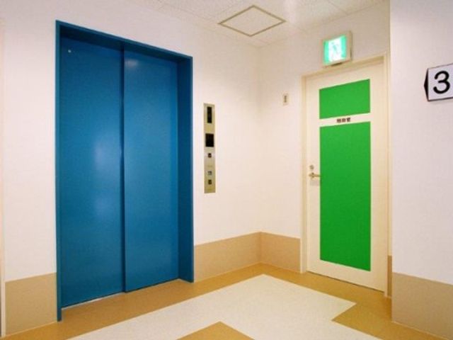 青いエレベーターと緑のドア エレベーター 明るい色合いの廊下は、快適な移動をサポートします。広々としたスペースが確保され、どなたでも安心してお過ごしいただけます。