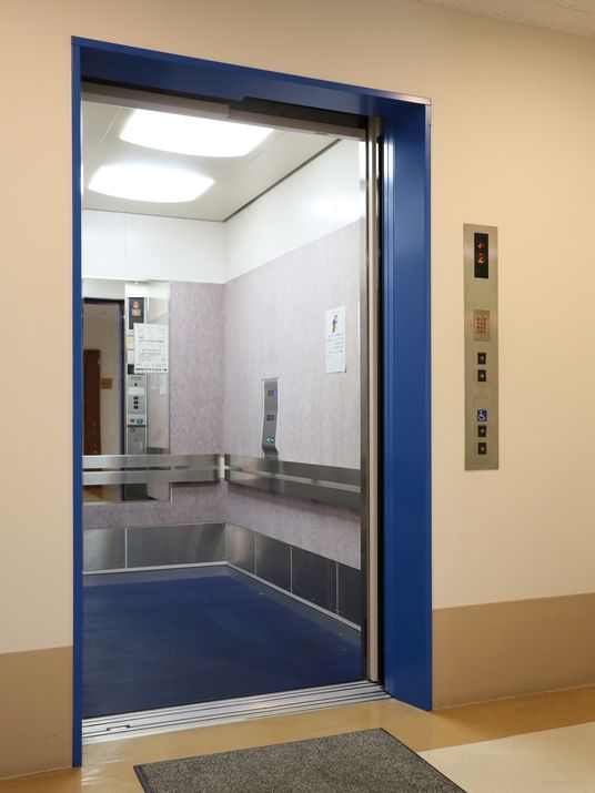 エレベーターは目立つように、入り口の扉付近と内部の床が濃いブルーで彩られている。縦長の大きな鏡と手すりが設置されている。