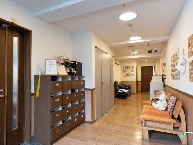暖かみのある廊下の様子 玄関 落ち着いた雰囲気の廊下には、くつろげるベンチやポストが備えられ、緑の植物や写真が居心地の良さを演出しています。