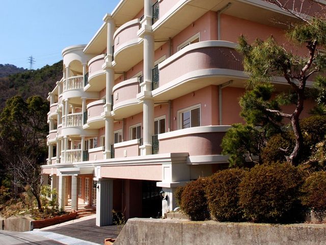 ピンクの外壁の建物エントランス 外観 開放的で設計されたエントランスは、明るく清潔感があります。周囲の緑豊かな環境も気持ちを和ませてくれるでしょう。
