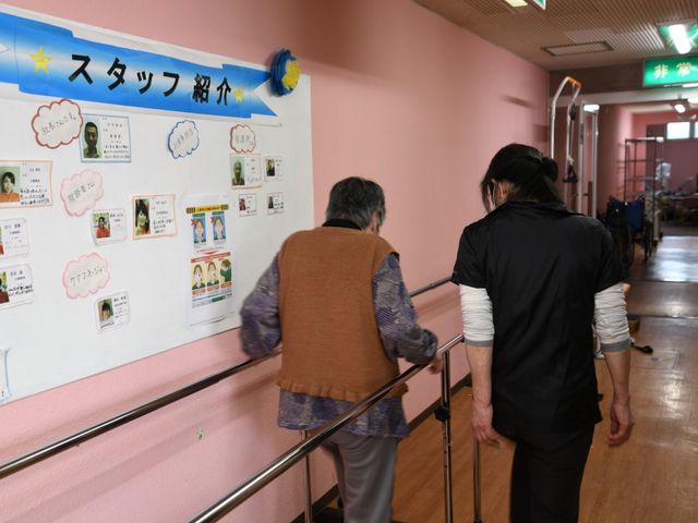 スタッフ紹介掲示物廊下 廊下 壁際にはスタッフ紹介が掲示されており、訪れる人の安心につながります。介助者と一緒に歩く姿が和やかな雰囲気を作り出しています。