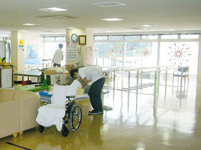 自然光が入る広々とした部屋 内観 大きな窓から自然光が差し込む明るい室内です。スタッフが利用者をサポートする姿があります。