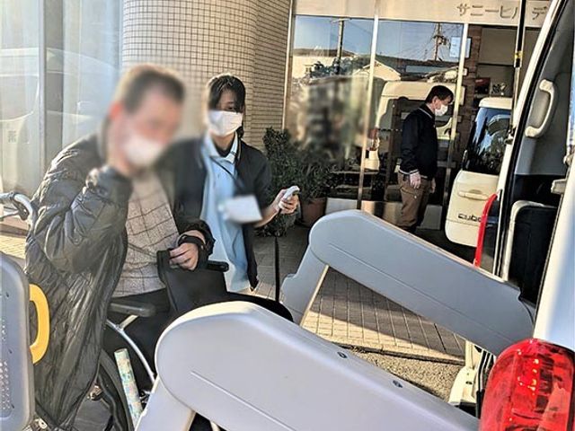 スタッフイメージ エントランス スタッフが利用者の乗車を支援しています。笑顔での対応が心地よい雰囲気を作り出しています。