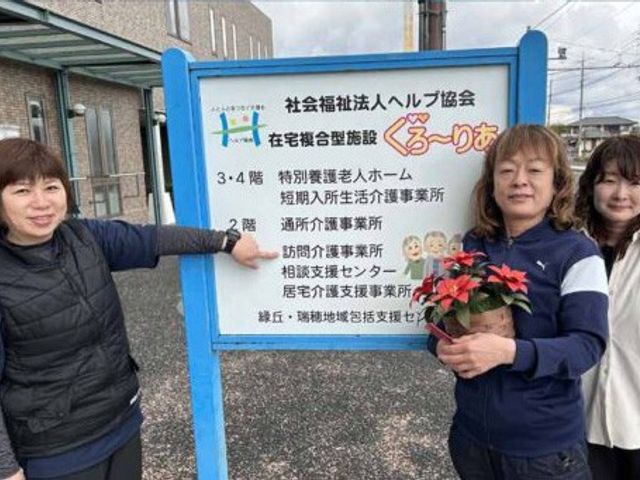 看板を持つスタッフ 看板 看板前でスタッフが活動内容を紹介しています。施設の雰囲気を知る一助となります。