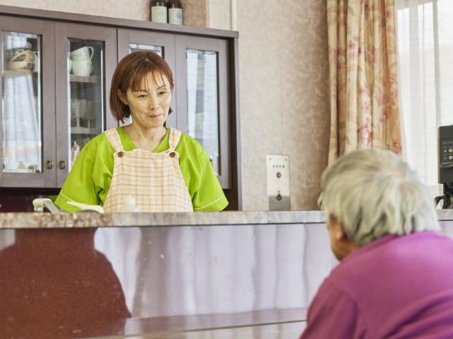 スタッフと利用者の会話 スタッフイメージ 明るい笑顔で対応するスタッフがいる様子です。温かみのある対話が、安心感を与えてくれます。