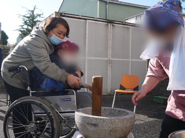 車椅子の方が餅つき活動 中庭 青空の下、車椅子の方が餅つきを体験しています。温かい交流の場として親しまれています。