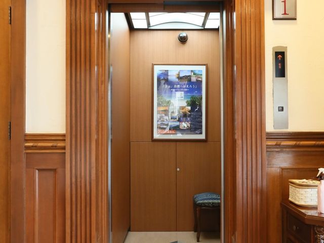 クラシカルなエレベーター前 エレベーター 落ち着いた雰囲気のエレベーター前です。木目調の装飾が施されており、心地よい環境でお迎えいたします。