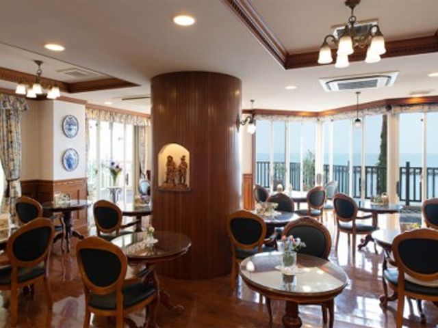 落ち着いた雰囲気のダイニング 食堂 広々としたダイニングでのひとときを、木のぬくもり感じながらご提供いたします。窓越しの光が優しく差し込む空間で、利用者様が心地よい食事の時間を過ごされています。