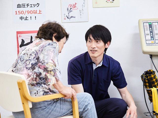 血圧チェック中の部屋 機能訓練室 職員が親身に利用者とコミュニケーションを取っています。安心して働ける環境です。