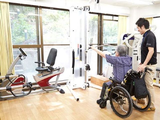 トレーニング機器と利用者とスタッフの多目的室 多目的室 自然光が差し込む中で、スタッフが利用者をサポートしながらトレーニングができる環境です。