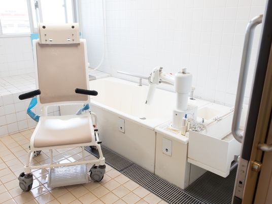 手すり付きの介護用浴槽と入浴用の車椅子が備え付けられている清潔な浴室。浴室の扉は引き戸となっている。