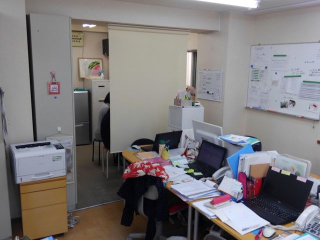 事務作業の様子のオフィス スタッフイメージ デスクに書類が並ぶ仕事空間です。職員が書類整理や電話対応を行っています。