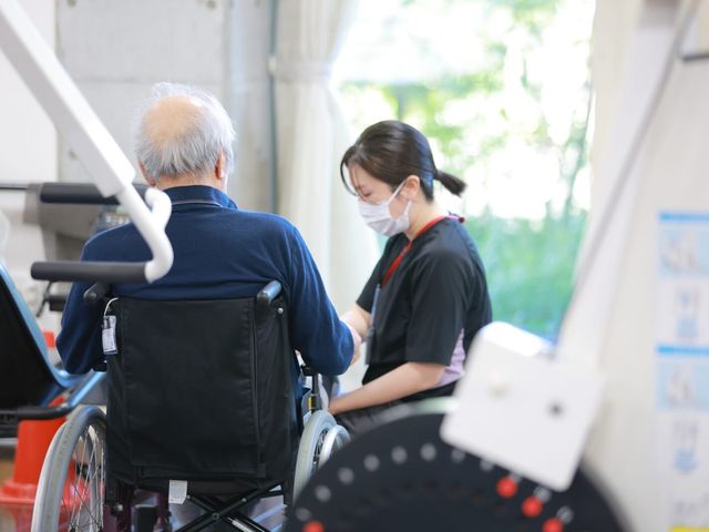 車椅子で訓練を受ける場面 機能訓練室 自然光が入る明るい空間で、車椅子利用者への丁寧なサポートが行われています。