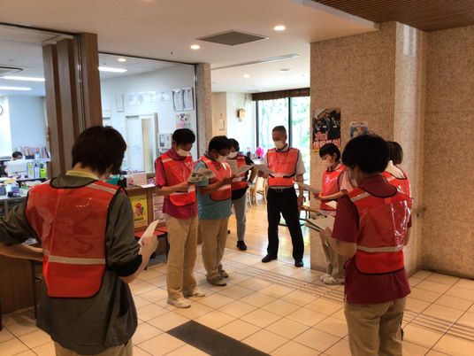 赤いベストの職員が集まるロビー  