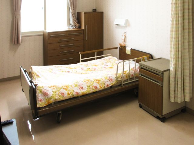 明るい居室のベッド 居室   窓から光が入る、落ち着いた雰囲気の居室です。ベッド周りに手すりや収納があり、働く場として動線を確認しやすい空間です。