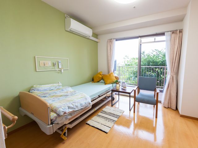 明るい居室の一角 居室 窓から光が差し込む居室は、機能的なベッドとリラックスできるチェアが配置され、快適な個人の空間を提供しています。