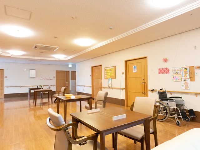 ゆったり明るい食堂空間 共有スペース ゆったりしたテーブル配置で、利用者が安心して食事や交流が楽しめる食堂です。壁には利用者の作品が飾られ、アットホームな雰囲気が漂っています。