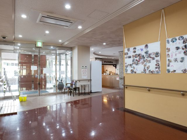エントランスの広々とした空間 玄関 広々とした明るいエントランスは、訪れる人々を温かく迎え入れます。壁には利用者の笑顔の掲示物が飾られ、心地よい第一印象を与えてくれるでしょう。
