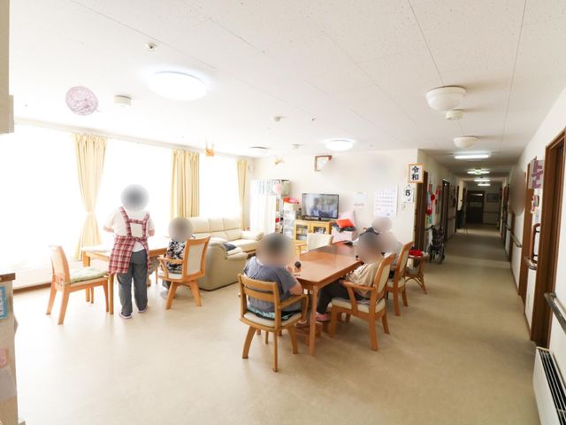 共有スペースでのふれあい風景 食堂 居心地の良いラウンジでは、職員が利用者の方々と会話を楽しんでいます。この明るく開放的な空間で、毎日のコミュニケーションが花開きます。