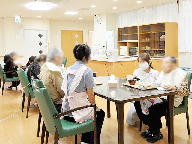 食事を楽しむリビング リビング 自然光が差し込むリビングで、利用者とスタッフが和やかに会話を楽しんでいます。