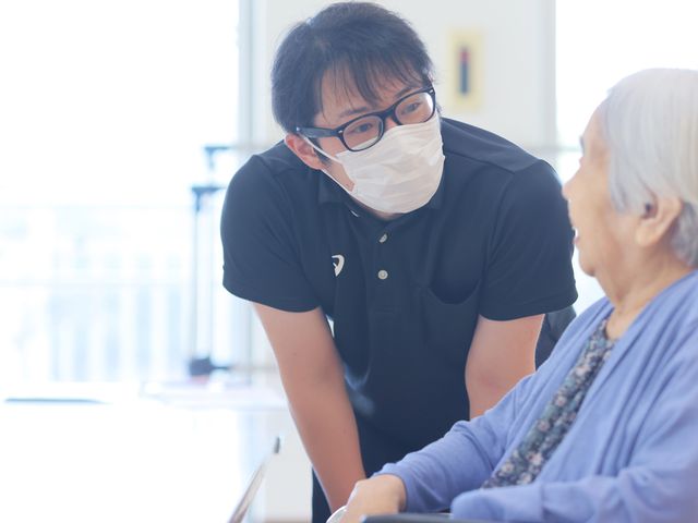 笑顔で話すスタッフと利用者 スタッフイメージ スタッフと利用者が笑顔で会話を楽しむ和やかなシーンです。信頼関係を築ける職場です。