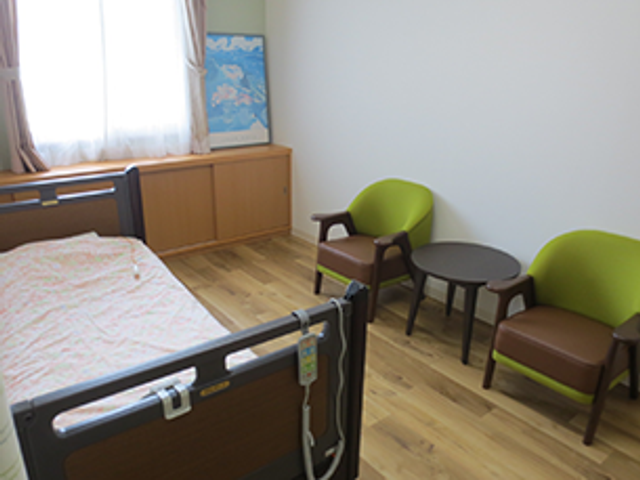 明るい居室の家具 居室   窓から光が入る、木目調の落ち着いた居室です。椅子と小さなテーブルがあり、くつろぎやすい雰囲気です。