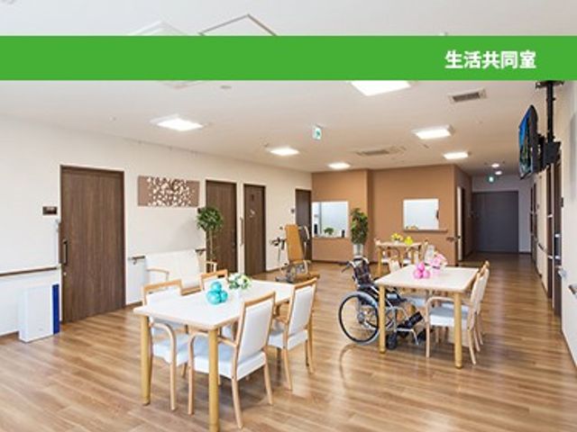 生活共有室 リビング   明るい木目調の空間に、テーブルと椅子がゆったり配置されています。車椅子でも移動しやすそうな広さがあり、落ち着いて過ごせます。