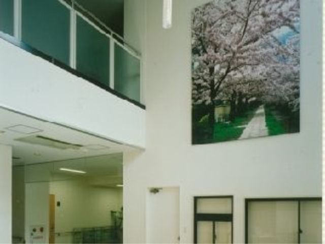 桜の絵が飾られた廊下 エントランスホール 開放的な廊下には、春を感じさせる桜の絵があり、訪れる人々に温かな印象を与えています。明るく落ち着いた環境は、働く上でも心地よいでしょう。